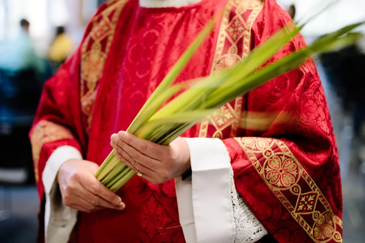 Padre católico com paramentos vermelhos segurando ramos de palmeira no Domingo de Ramos
